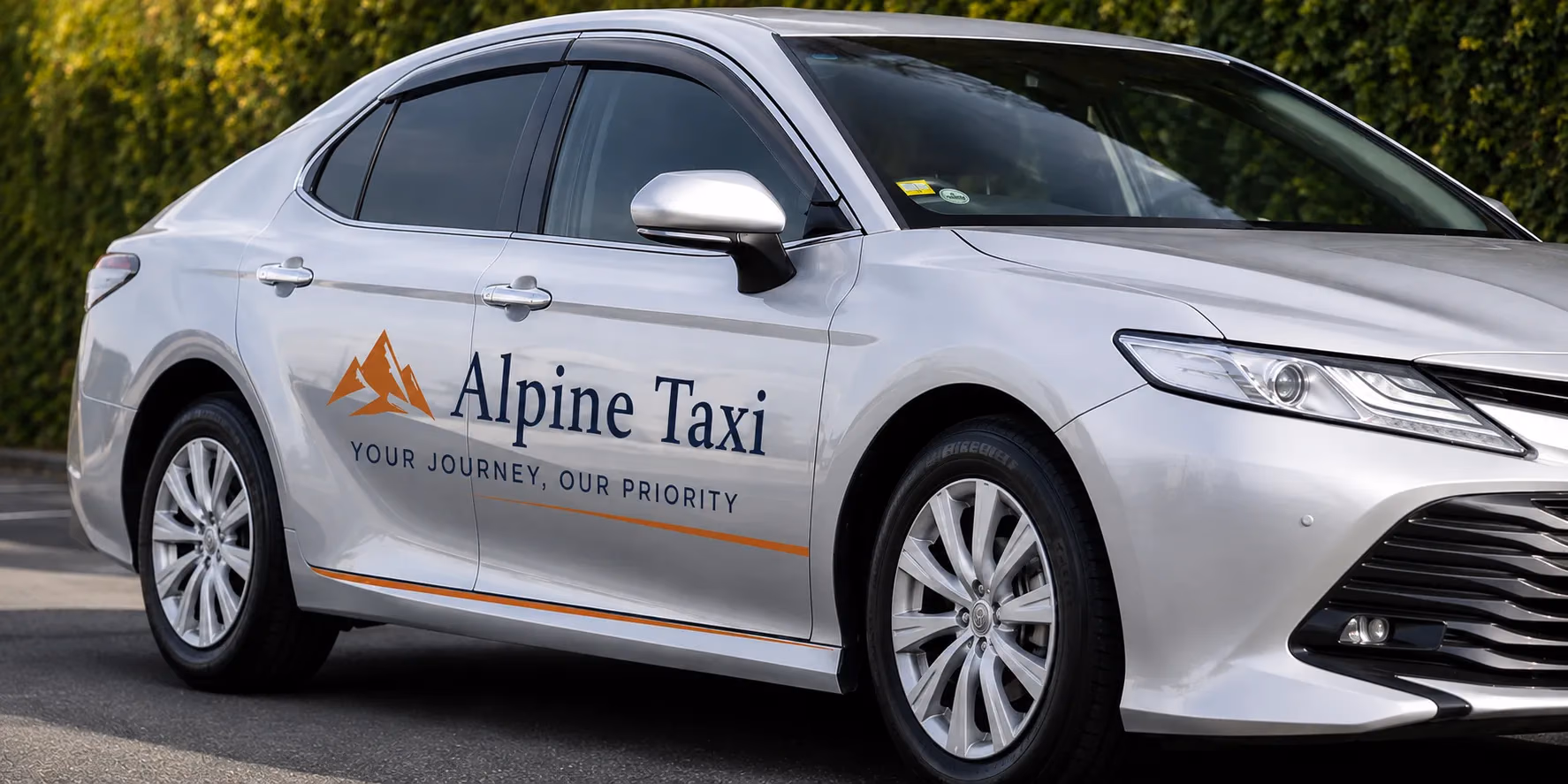 An Alpine Taxi silver sedan parked beside a hedge in Queenstown